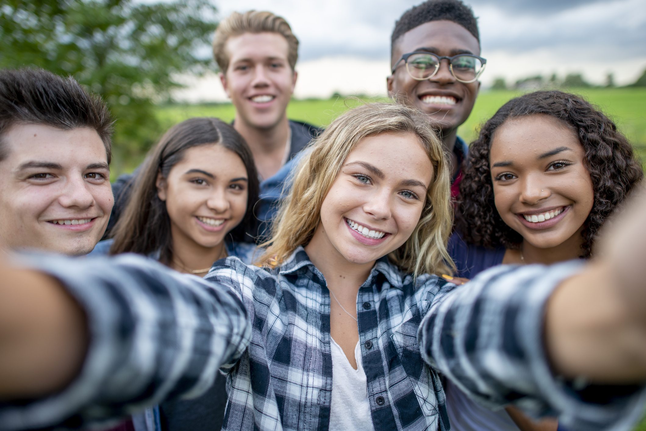 A group of multi-ethnic students taking a selfie outside.  They are dressed casually and having fun together in a group.