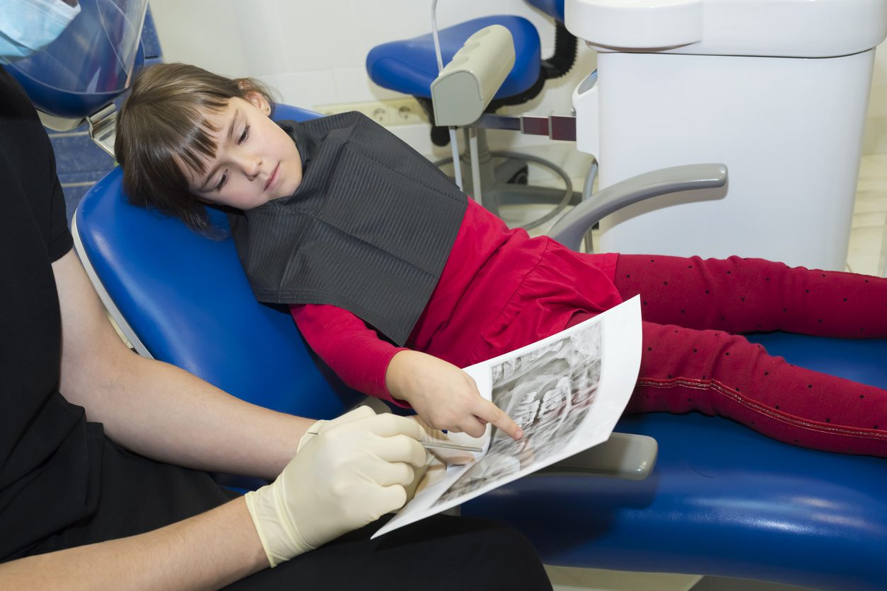 A dentist showing dental X-rays (radiographs) to a patient, a kid.